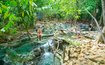Visitors relaxing in the Emerald Pool Hot Springs surrounded by lush greenery in Krabi, Thailand.