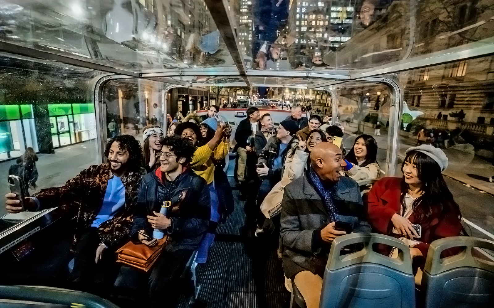 Tourists enjoying a night city view from an open-top bus on a hop-on hop-off tour.