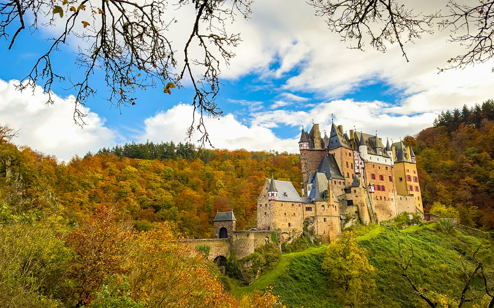 Schloss Eltz im Vordergrund und Bäume mit buntem Herbstlaub im Hintergrund