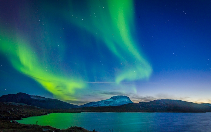 Northern lights over a mountain landscape with a lake in the foreground.