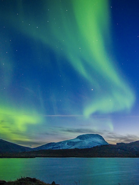 Northern lights over a mountain landscape with a lake in the foreground.