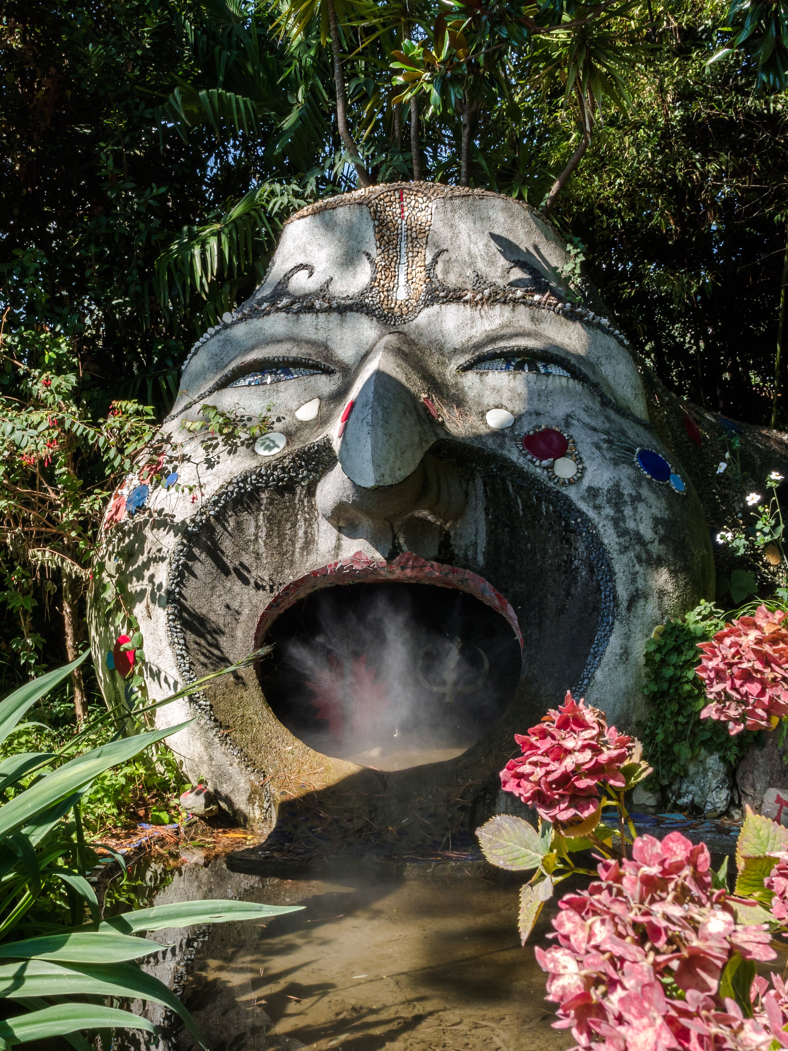 Sculpture with open mouth and steam in ANIMA Garden, Marrakech, surrounded by lush plants.
