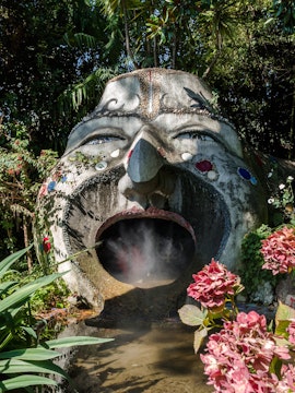 Sculpture with open mouth and steam in ANIMA Garden, Marrakech, surrounded by lush plants.