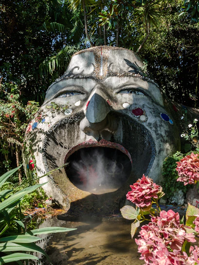 Sculpture with open mouth and steam in ANIMA Garden, Marrakech, surrounded by lush plants.