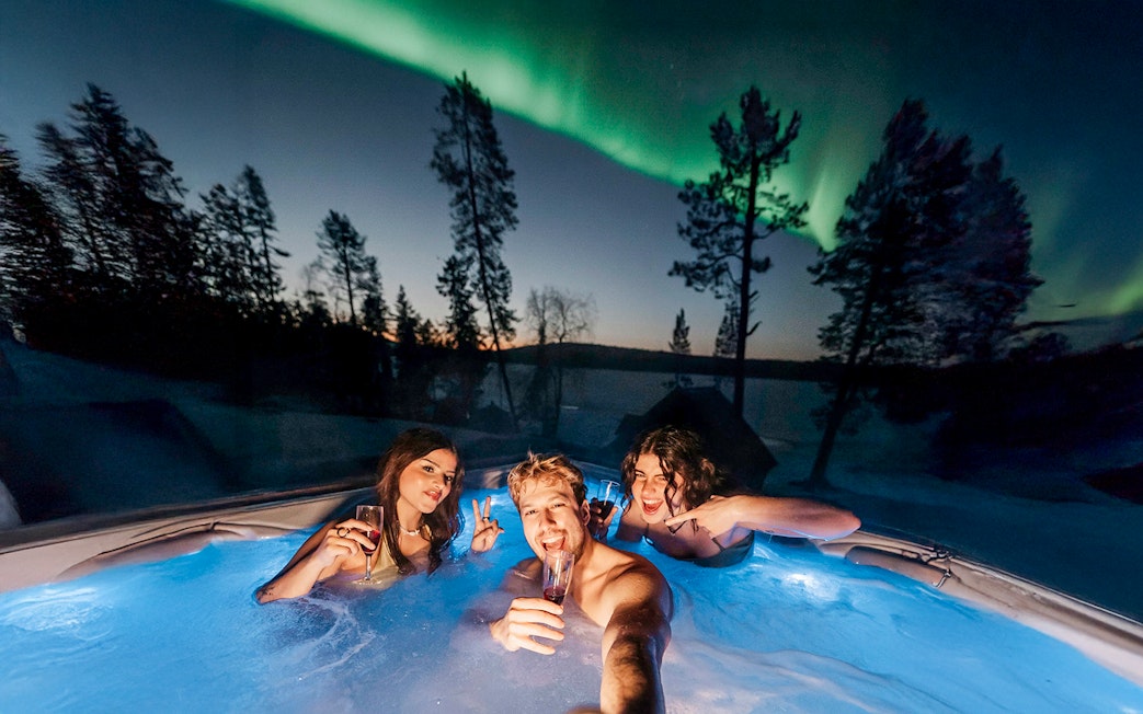 Guests in hot tub under Northern Lights in Rovaniemi sauna experience.