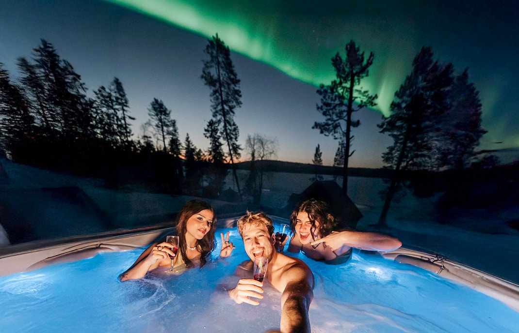 Guests in hot tub under Northern Lights in Rovaniemi sauna experience.