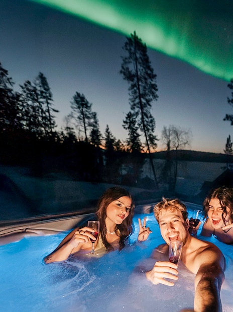 Guests in hot tub under Northern Lights in Rovaniemi sauna experience.
