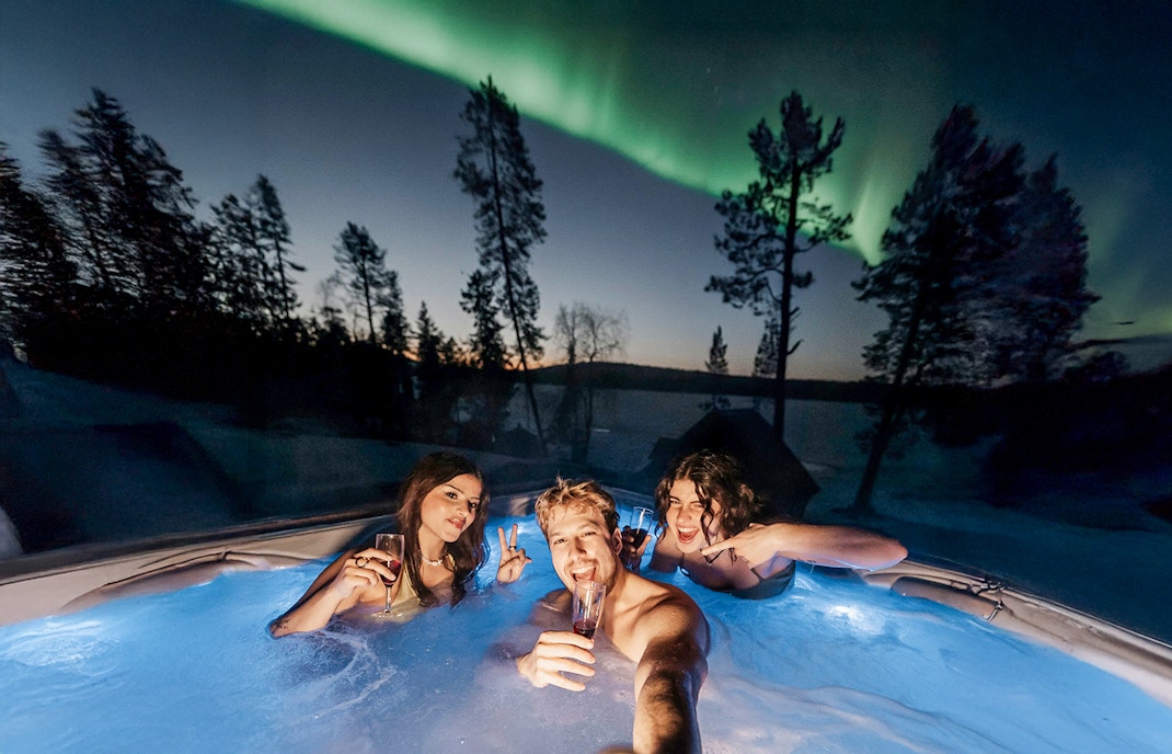 Guests in hot tub under Northern Lights in Rovaniemi sauna experience.