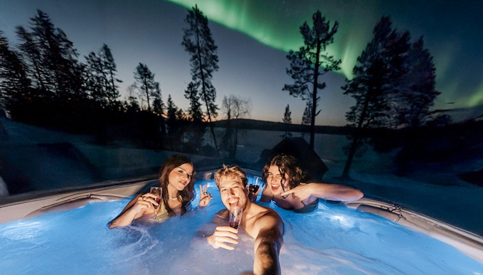 Guests in hot tub under Northern Lights in Rovaniemi sauna experience.