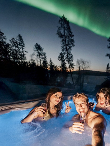 Guests in hot tub under Northern Lights in Rovaniemi sauna experience.