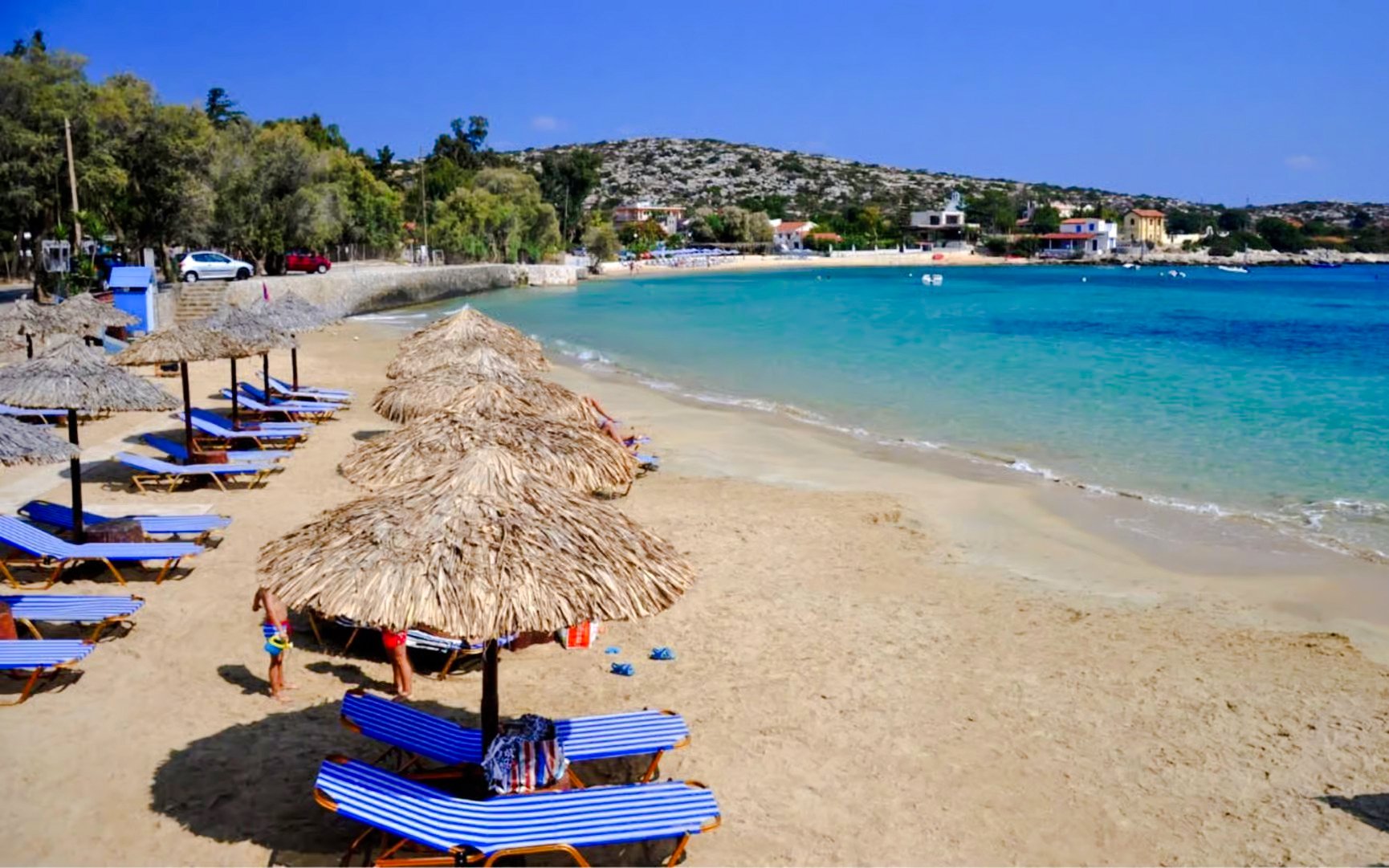 Sun loungers and umbrellas on Marathi Beach, Crete, with clear blue water and distant hills.