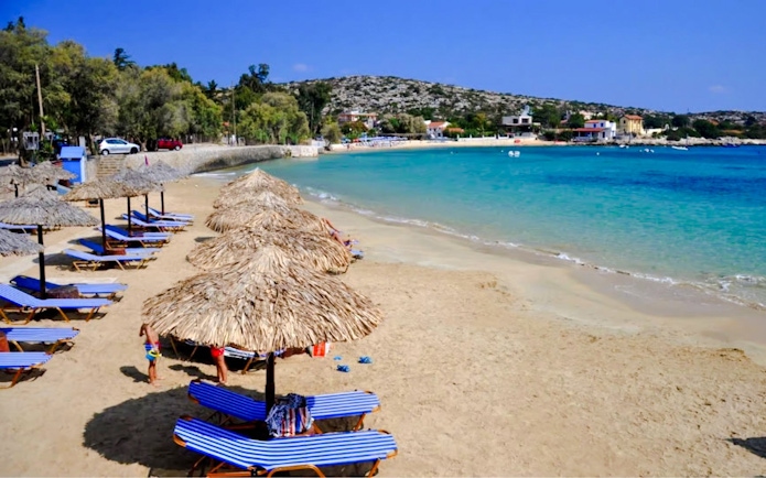 Sun loungers and umbrellas on Marathi Beach, Crete, with clear blue water and distant hills.