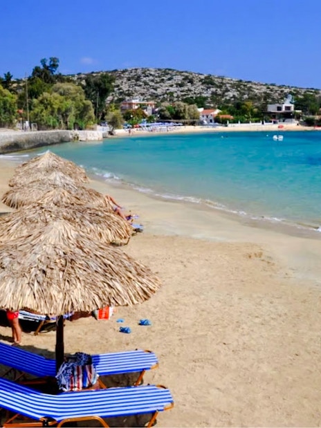 Sun loungers and umbrellas on Marathi Beach, Crete, with clear blue water and distant hills.