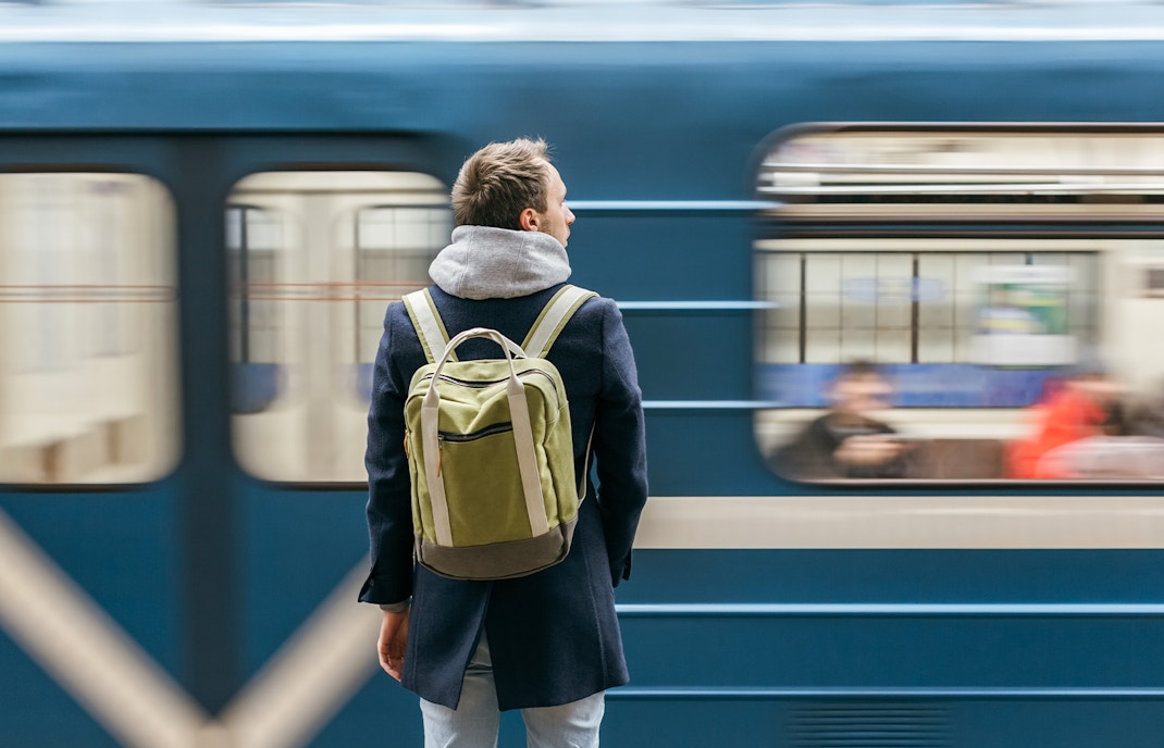 Man with backpack standing at a train station as a train passes by.