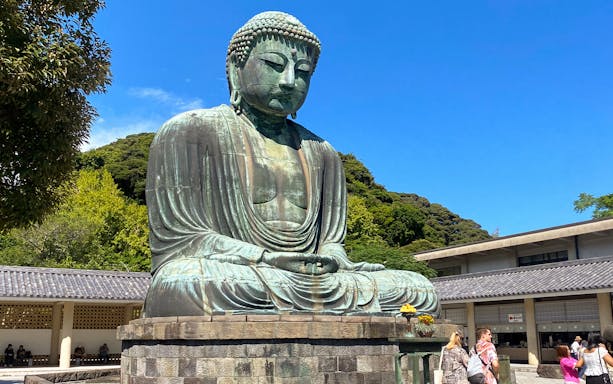 Big Buddha statue in Kamakura, Japan, surrounded by trees and visitors.