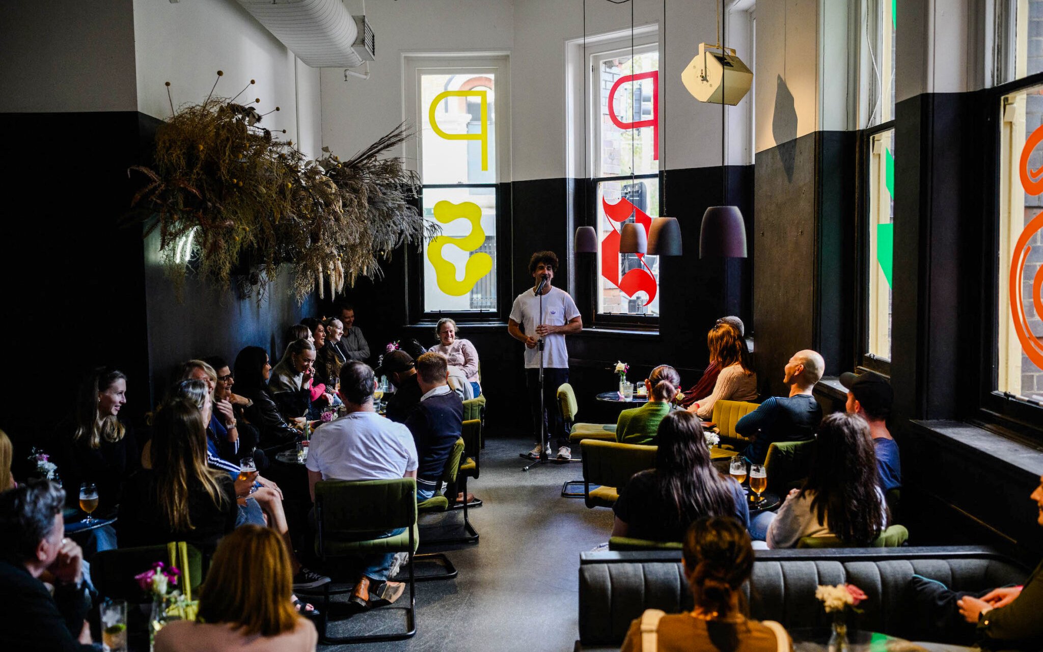 Stand-up comedian performing at Sydney Comedy Festival in a cozy venue with audience seated.