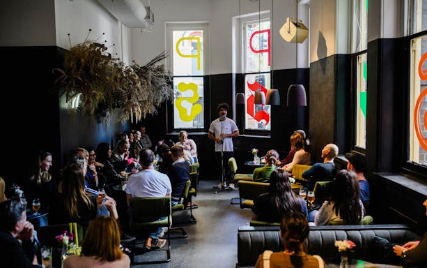 Stand-up comedian performing at Sydney Comedy Festival in a cozy venue with audience seated.