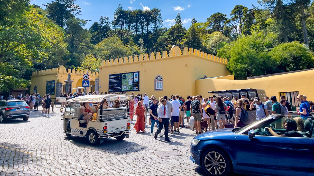 Crowd outside Sintra National Palace entrance with parked cars, Portugal.