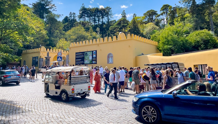 Crowd outside Sintra National Palace entrance with parked cars, Portugal.