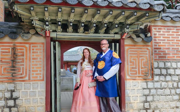 Couple in traditional Korean attire at a historic gate in Seoul.