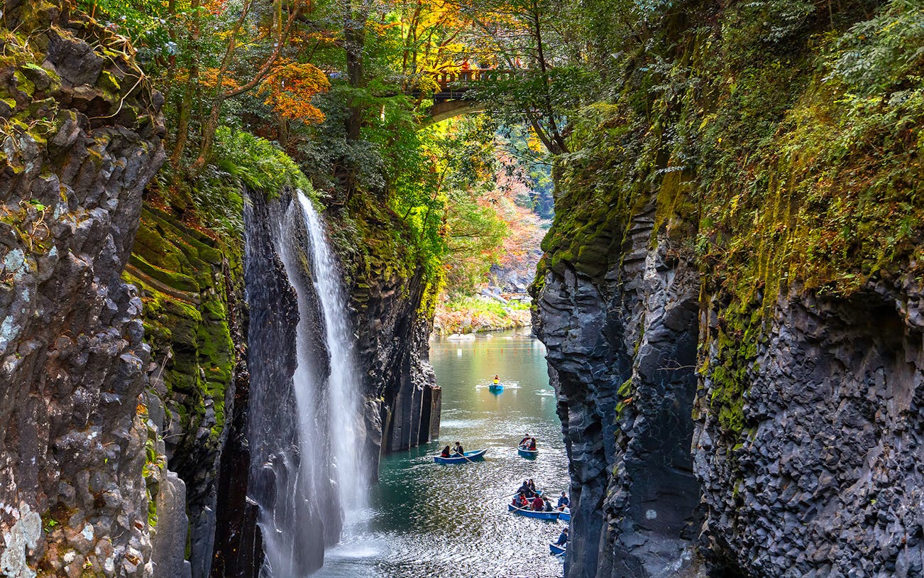 Boats in Takachiho Gorge with waterfall and bridge, Miyazaki, Japan.