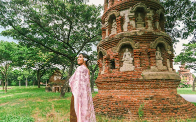 Person in traditional attire near ancient brick stupa with Buddha statues, Ancient City tour.