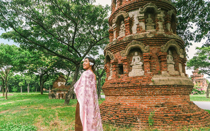 Person in traditional attire near ancient brick stupa with Buddha statues, Ancient City tour.