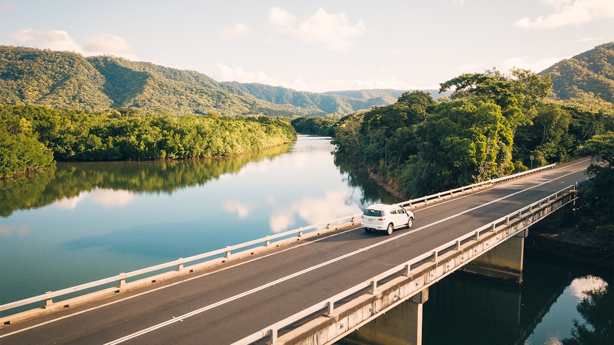 Car crossing a bridge over a river in Daintree National Park, surrounded by lush greenery.