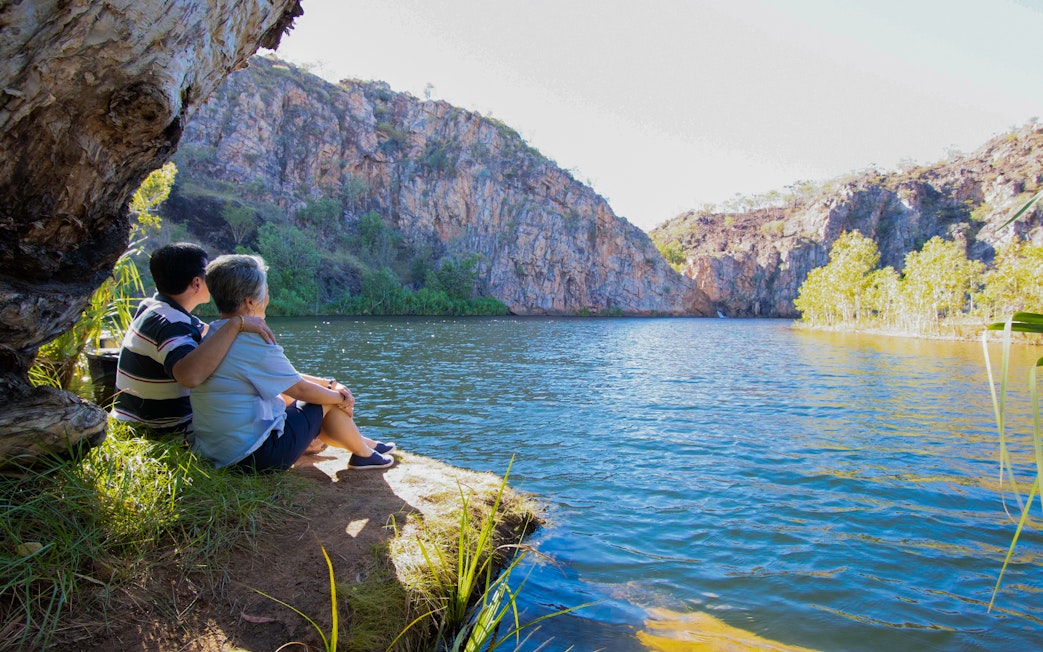Couple sitting by Katherine Gorge, enjoying the view of cliffs and water during a guided tour.