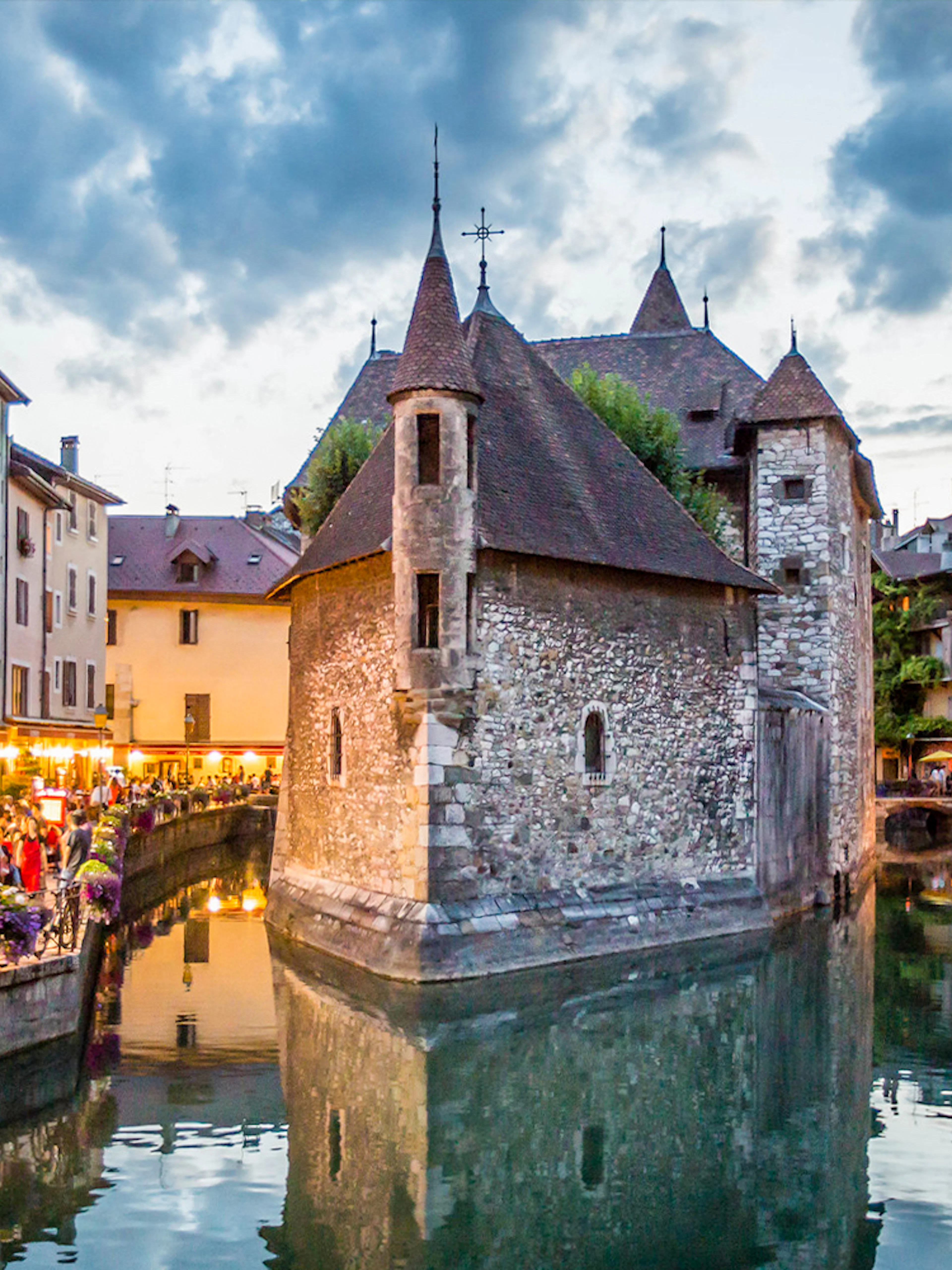 Annecy canal with historic buildings and evening lights reflecting on water.