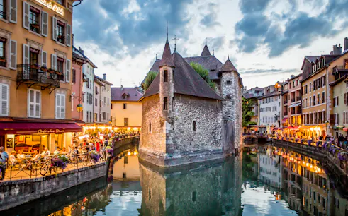 Annecy canal with historic buildings and evening lights reflecting on water.