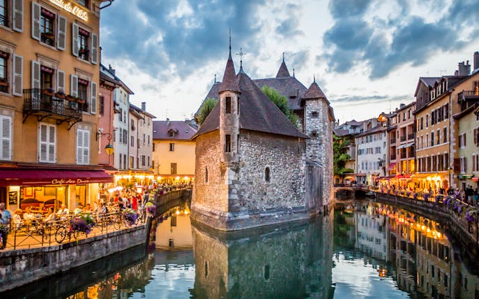 Annecy canal with historic buildings and evening lights reflecting on water.