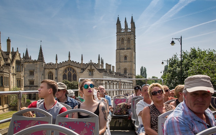 Open-top bus tour with tourists viewing historic Oxford architecture.