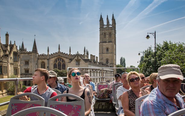 Open-top bus tour with tourists viewing historic Oxford architecture.