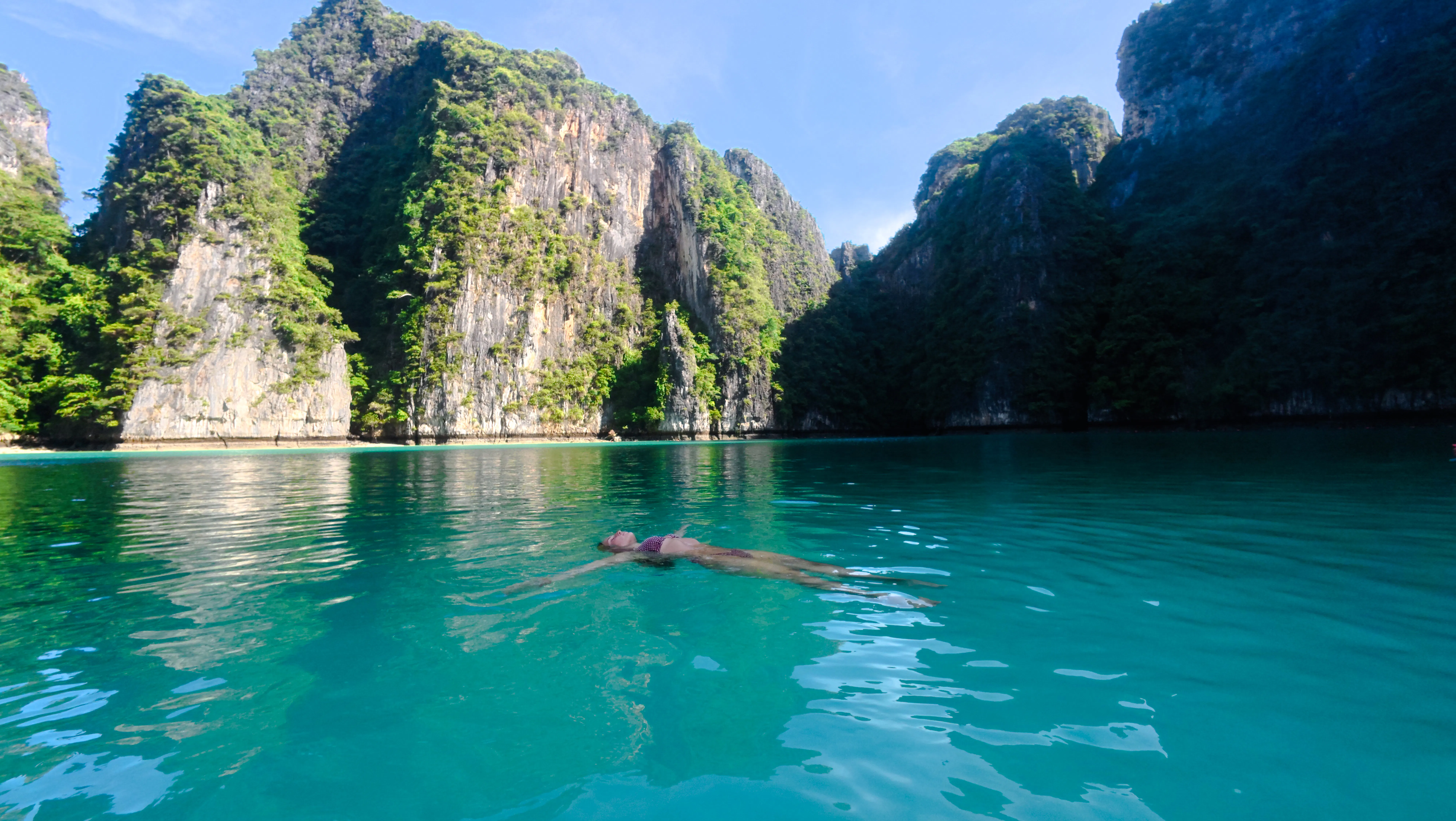 Person floating in turquoise water surrounded by limestone cliffs, Krabi.