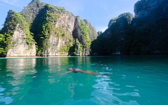 Person floating in turquoise water surrounded by limestone cliffs, Krabi.
