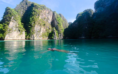 Person floating in turquoise water surrounded by limestone cliffs, Krabi.
