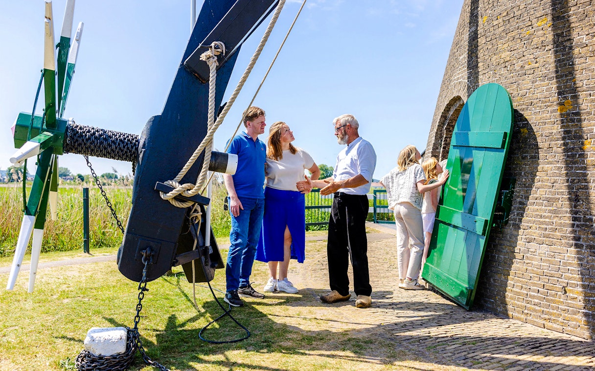 Family learning about windmills at Kinderdijk, Netherlands, with a guide explaining the mechanism.