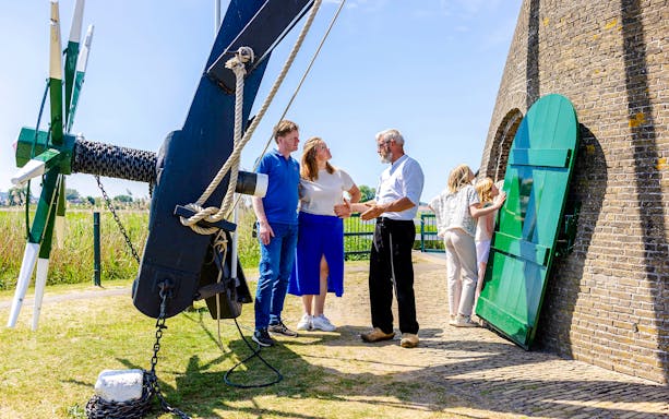 Family learning about windmills at Kinderdijk, Netherlands, with a guide explaining the mechanism.