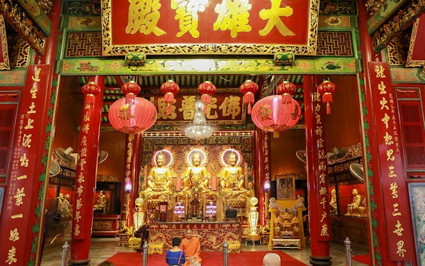 Buddhist temple interior in Bangkok with golden statues and red lanterns.