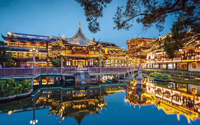 Yuyuan Gardens in Shanghai, China, illuminated at night with traditional architecture reflected in the pond.