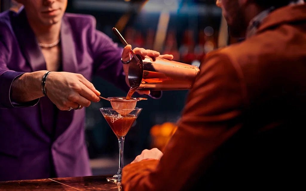 Bartender pouring cocktail through strainer during workshop.