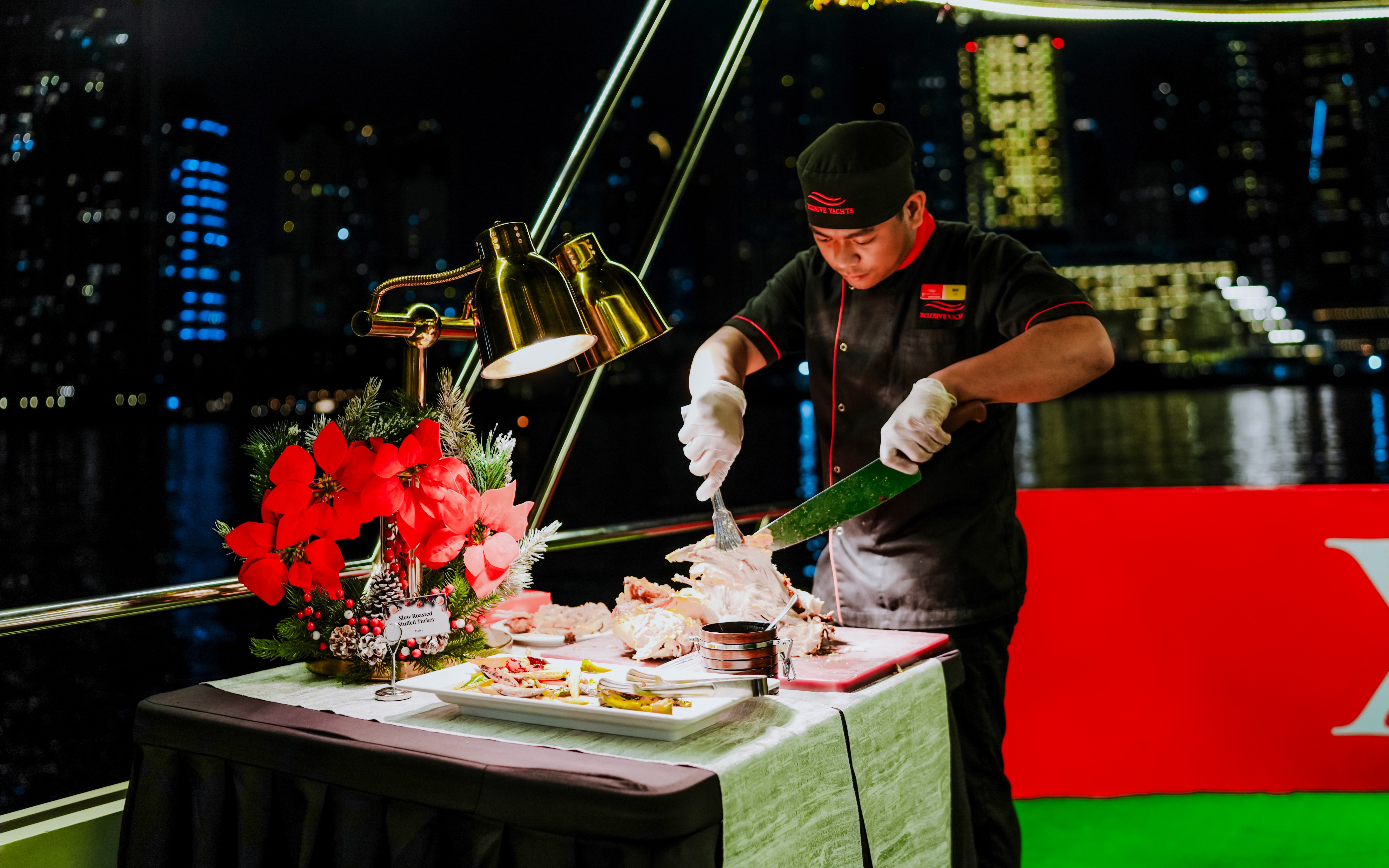 Chef carving turkey on a Christmas dinner cruise with city skyline in the background.