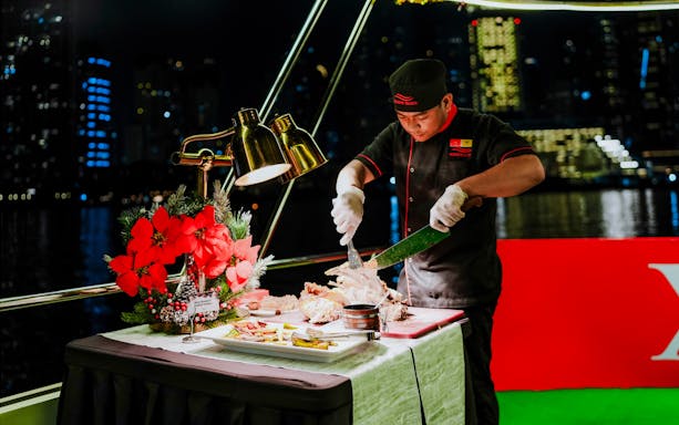 Chef carving turkey on a Christmas dinner cruise with city skyline in the background.