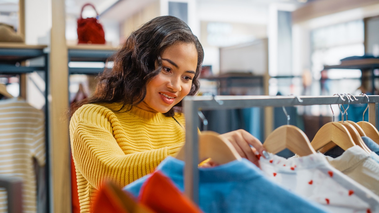 Female customer browsing clothes on hangers in a clothing store.