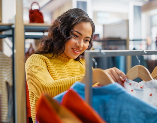 Female customer browsing clothes on hangers in a clothing store.