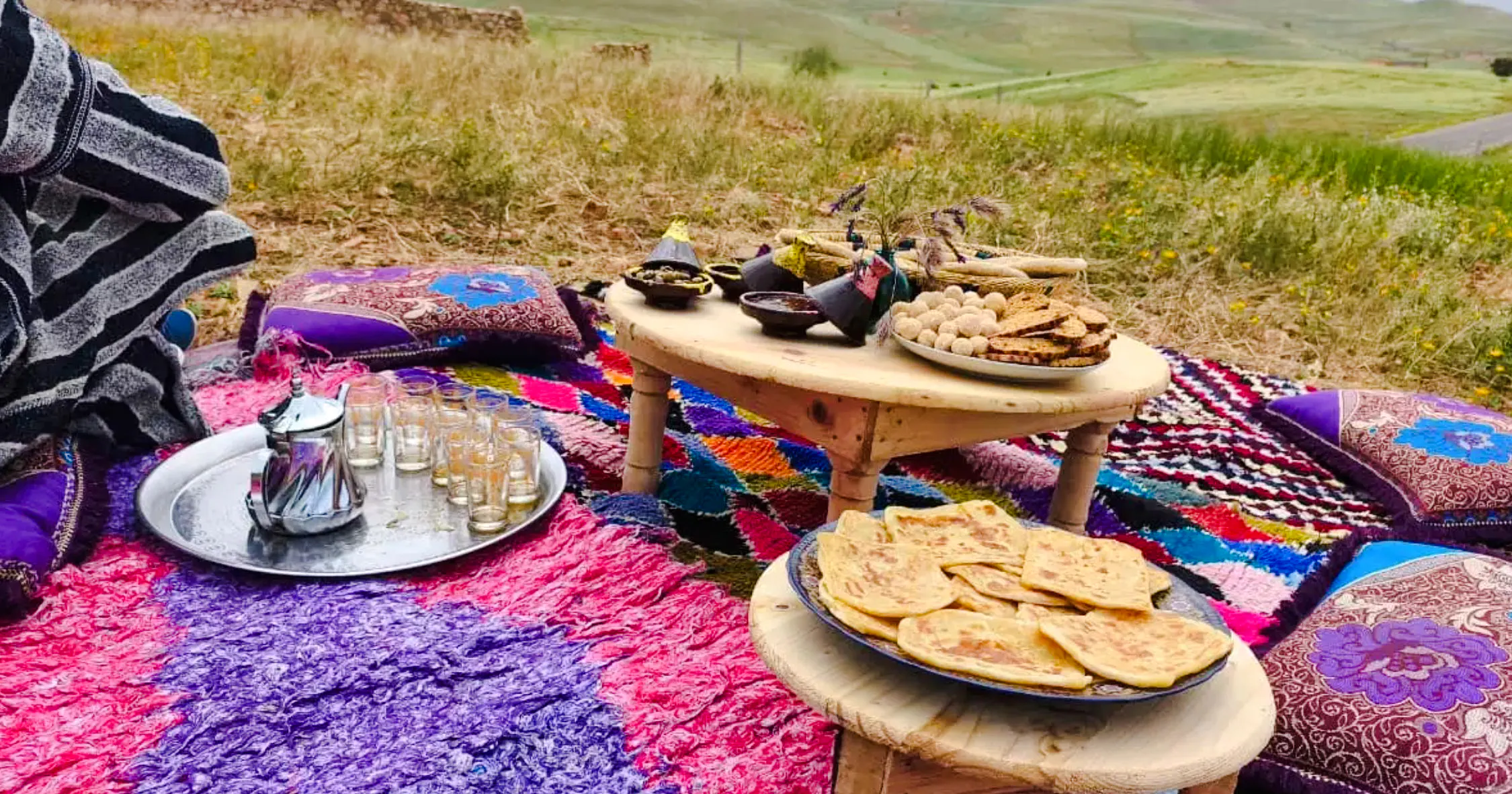 Traditional Moroccan tea setup with snacks on colorful rugs at Jebel Irhoud Archaeological Site.