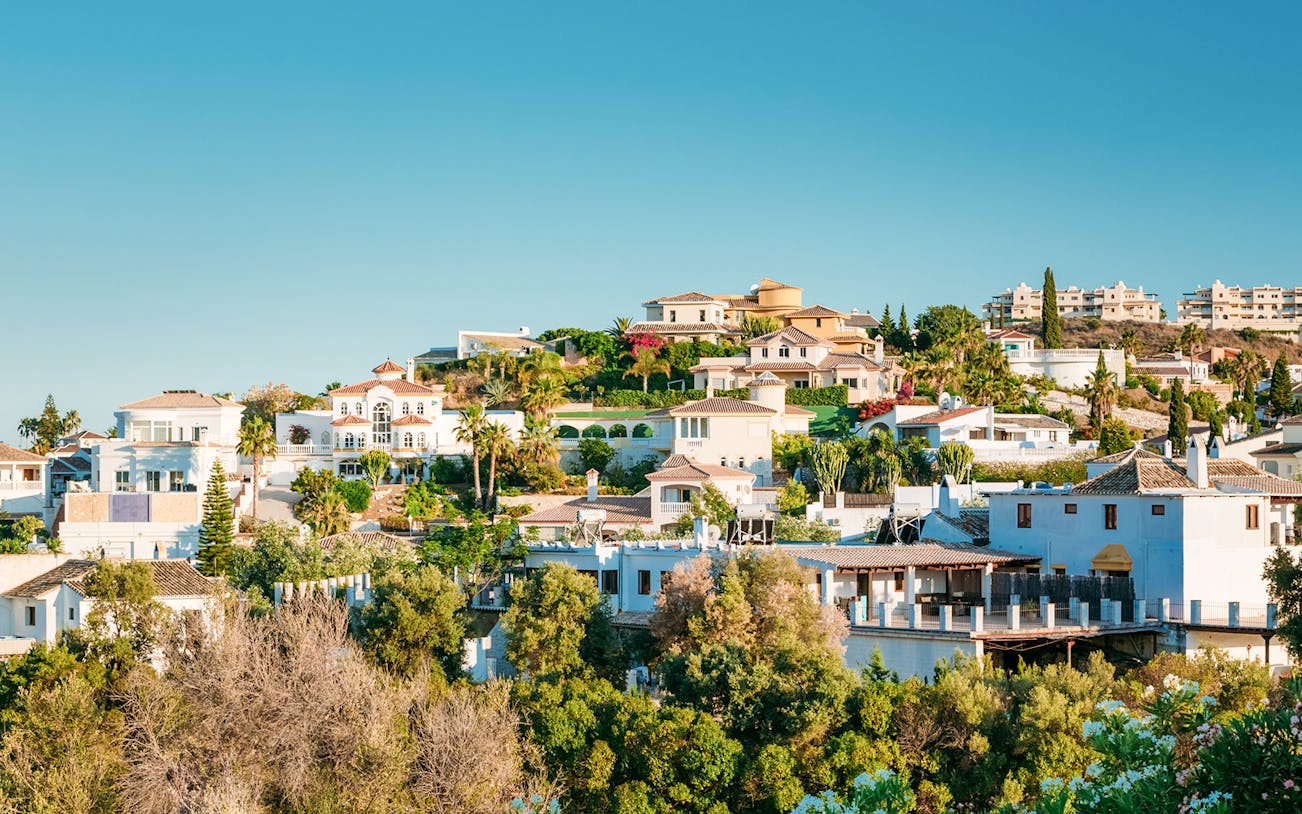 Hillside view of whitewashed houses in Mijas, Spain, surrounded by greenery.