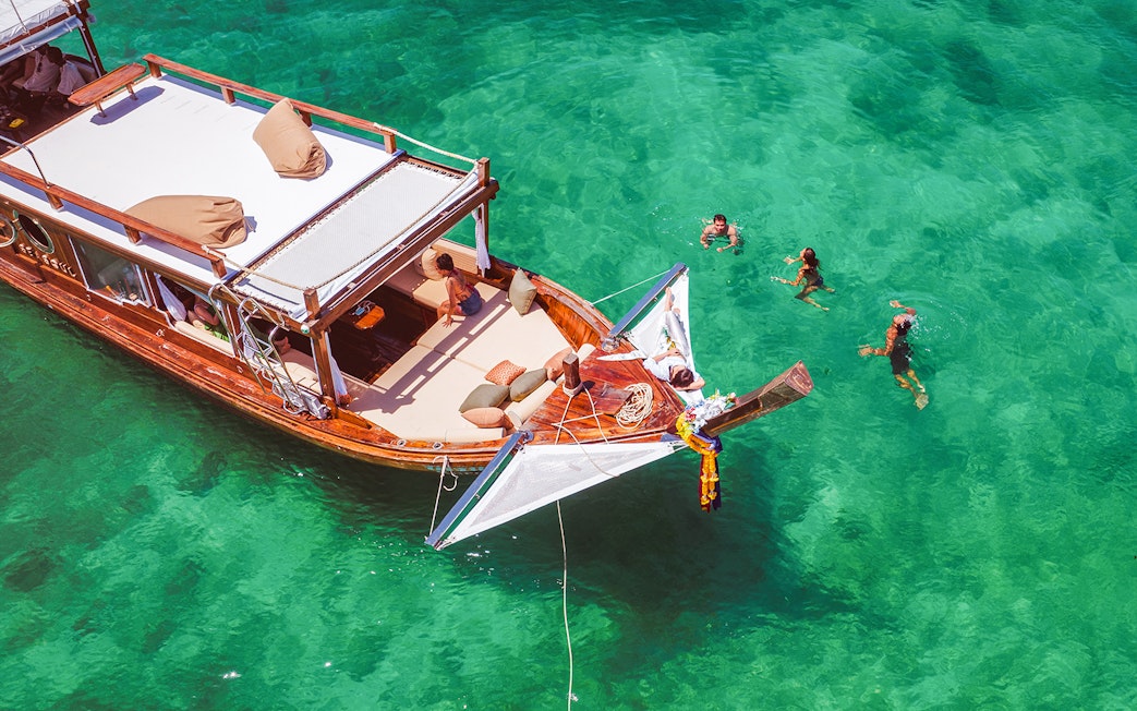 Luxury longtail boat with people swimming in turquoise waters, Krabi.