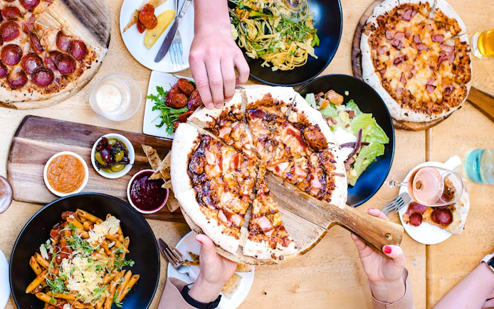 Frankie's on Rotto lunch spread with pizza, pasta, and salads on a wooden table.